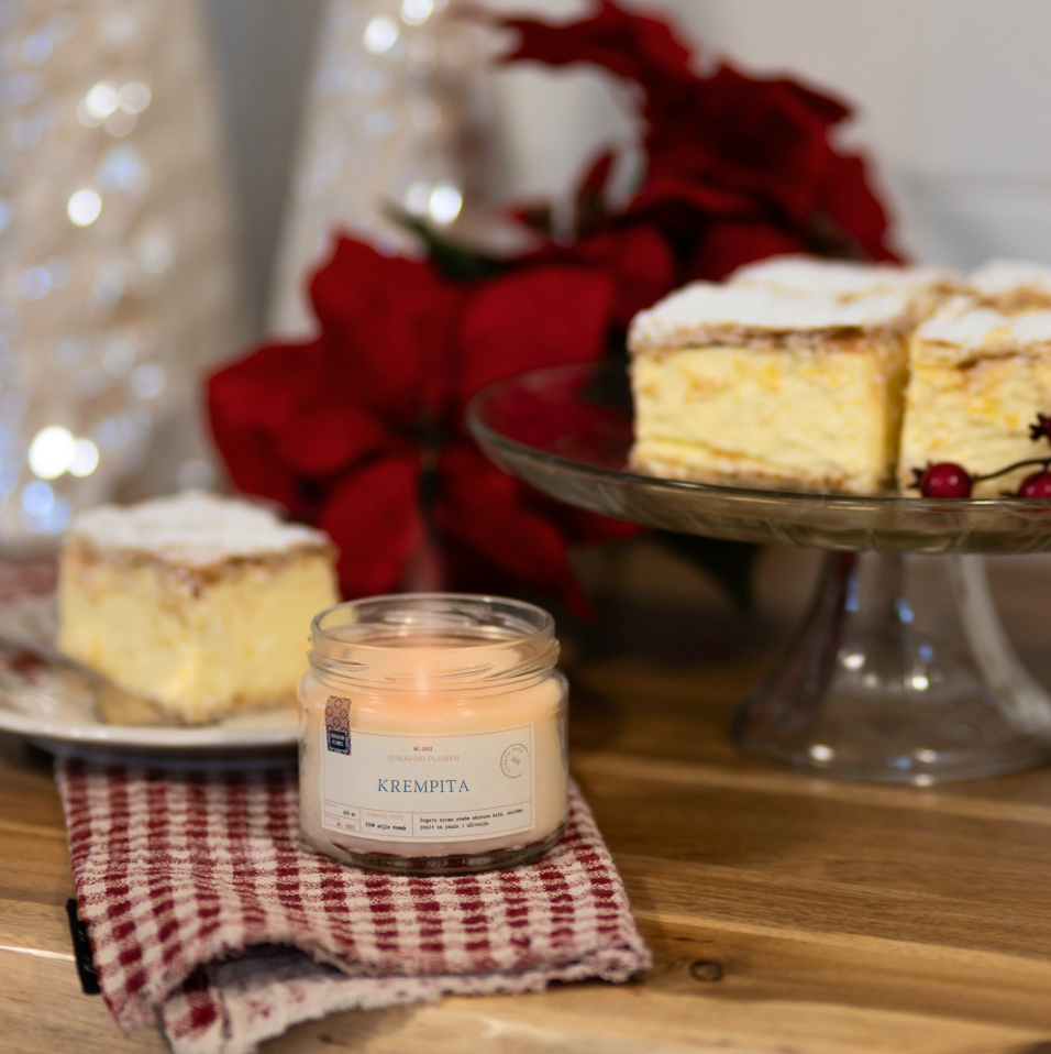 Mirisna sojina sveća Krempita iz kolekcije Ususkani Dani brenda Dunavski Plamen – ručno pravljena sveća sa slatkim mirisom vanile i kreme, inspirisana domaćim kolačem krempitom, uz praznični sto i božićnu dekoraciju.